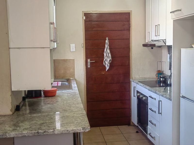 A functional kitchen featuring white cabinetry, laminate countertops, built-in oven and hob, and tiled flooring, providing a practical workspace for daily cooking.