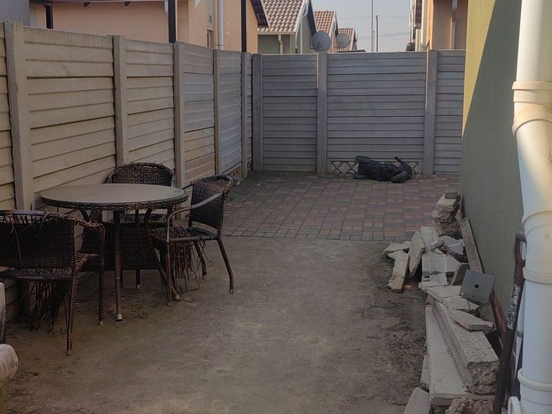 A rear courtyard area featuring a paved patio section, enclosed by precast concrete boundary walls and a functional downpipe.