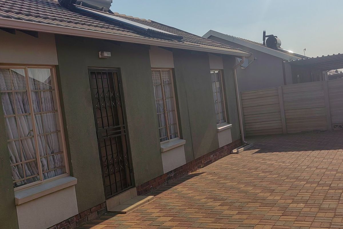 Rear exterior view of the house featuring a paved patio area, secure entrance, and perimeter precast walling.