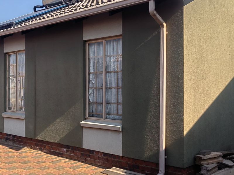Rear exterior view of the house featuring a paved patio area, solar water heating system, and well-maintained rendered walls with brick plinth detailing.