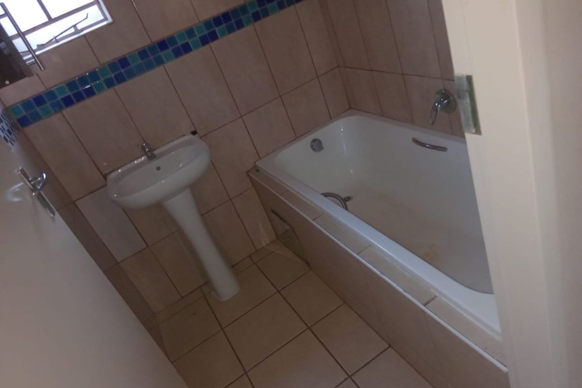 A functional bathroom featuring a pedestal basin and a built-in bathtub with tiled walls and flooring, requiring some cosmetic updates.