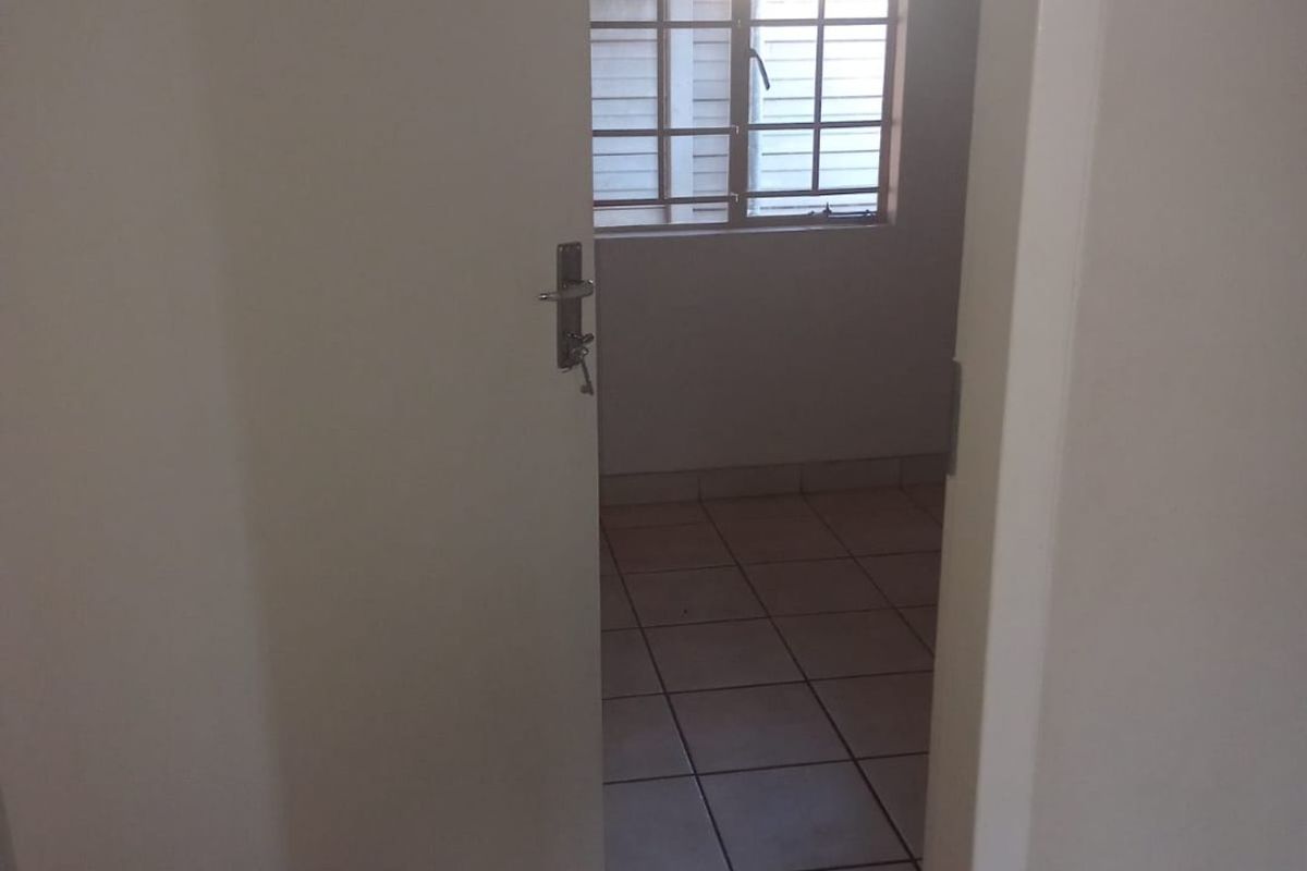 A view through an open doorway into an empty bedroom featuring tiled flooring and a window with security bars.