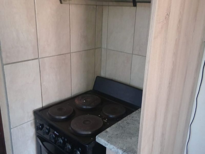 Compact kitchen area featuring a black electric stove, extractor fan, tiled splashback, and light wood-finish cabinetry with a stone-look countertop.