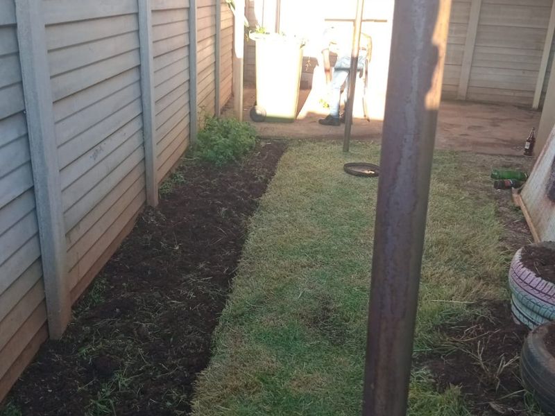A rear garden area featuring a precast concrete boundary wall and a small lawn section with a metal support structure.