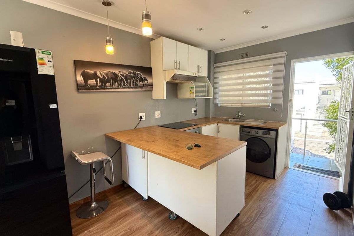 A functional kitchen featuring built-in cabinetry, wood-look laminate countertops, integrated hob, extractor fan, and direct access to an outdoor balcony area.