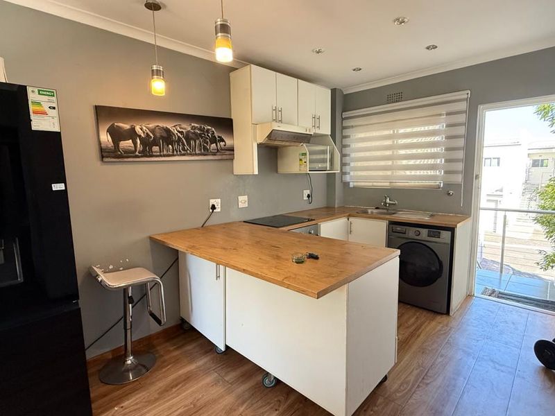 A functional kitchen featuring built-in cabinetry, wood-look laminate countertops, integrated hob, extractor fan, and direct access to an outdoor balcony area.