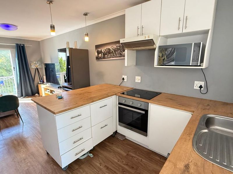 Open-plan living area featuring a modern kitchen with wooden countertops, built-in appliances, and direct access to a balcony through sliding glass doors.