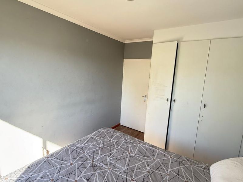 A bedroom featuring laminate flooring, built-in cupboards, and a neutral grey accent wall.