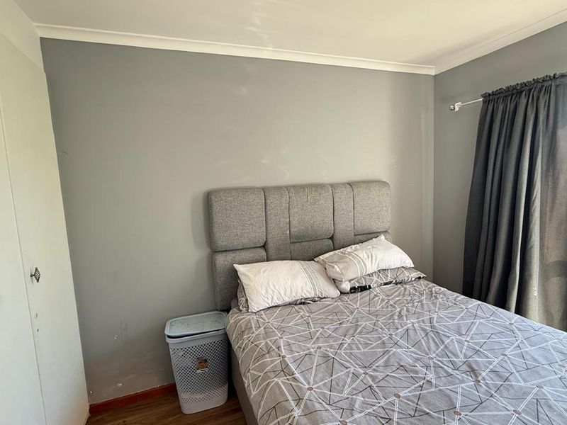 A functional bedroom featuring a built-in wardrobe, neutral grey walls, and a large window providing natural light.
