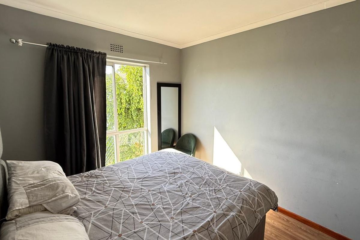 A bedroom featuring laminate flooring, neutral grey walls, and a sliding window providing natural light.