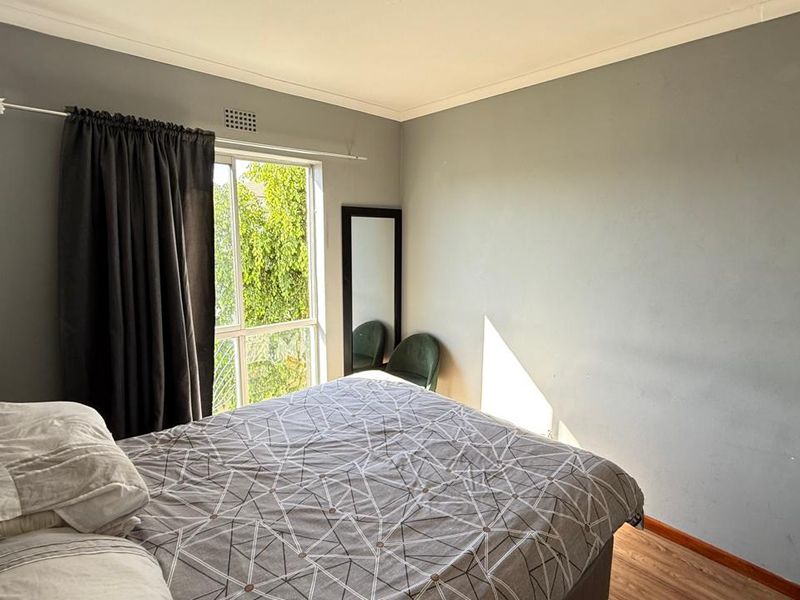 A bedroom featuring laminate flooring, neutral grey walls, and a sliding window providing natural light.