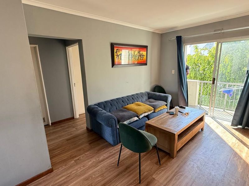 A living room featuring laminate flooring, neutral wall finishes, and a sliding glass door providing access to an outdoor balcony area.