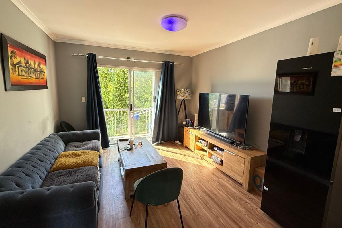A comfortable living room featuring laminate flooring and a sliding glass door that provides access to a balcony, allowing for natural light.