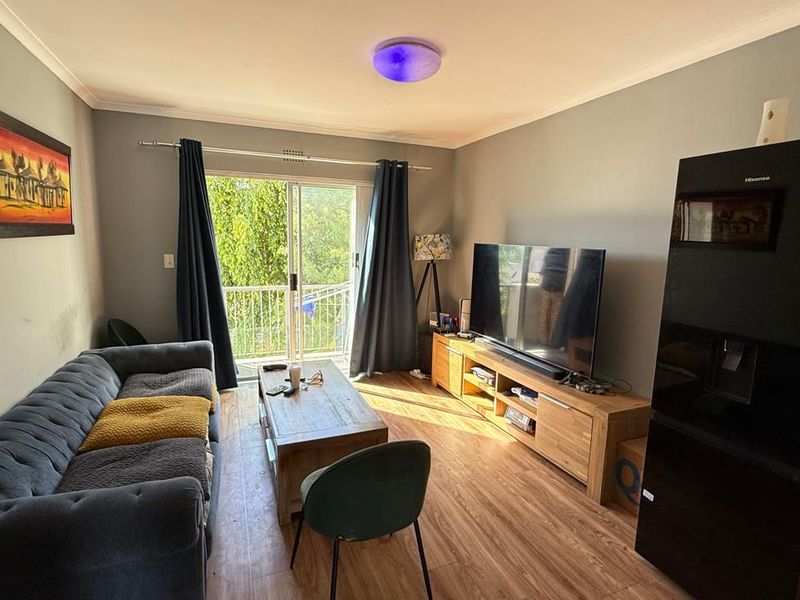 A comfortable living room featuring laminate flooring and a sliding glass door that provides access to a balcony, allowing for natural light.
