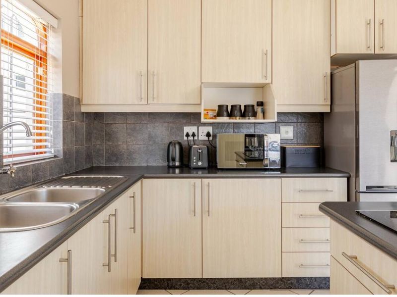 A functional kitchen featuring light wood-finish cabinetry, dark laminate countertops, a double stainless steel sink, and a tiled splashback.