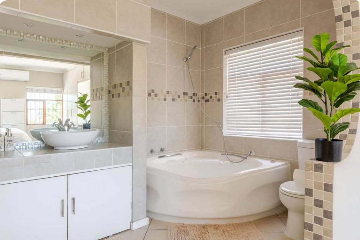 A well-maintained bathroom featuring a corner bathtub, a vanity with a vessel sink, and neutral wall tiling.