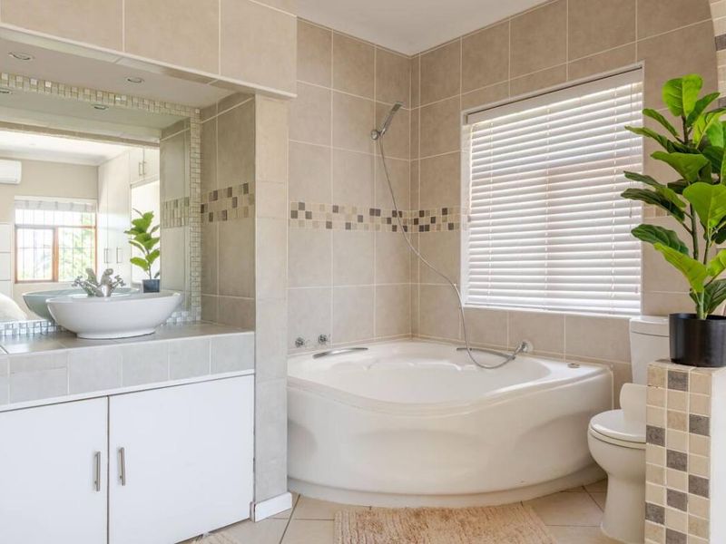 A well-maintained bathroom featuring a corner bathtub, a vanity with a vessel sink, and neutral wall tiling.
