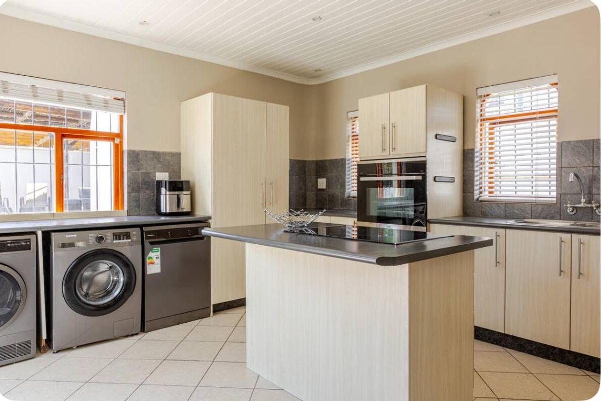 A functional kitchen featuring light wood cabinetry, dark laminate countertops, built-in oven and hob, tiled backsplash, and integrated laundry appliance space.
