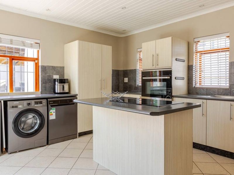 A functional kitchen featuring light wood cabinetry, dark laminate countertops, built-in oven and hob, tiled backsplash, and integrated laundry appliance space.