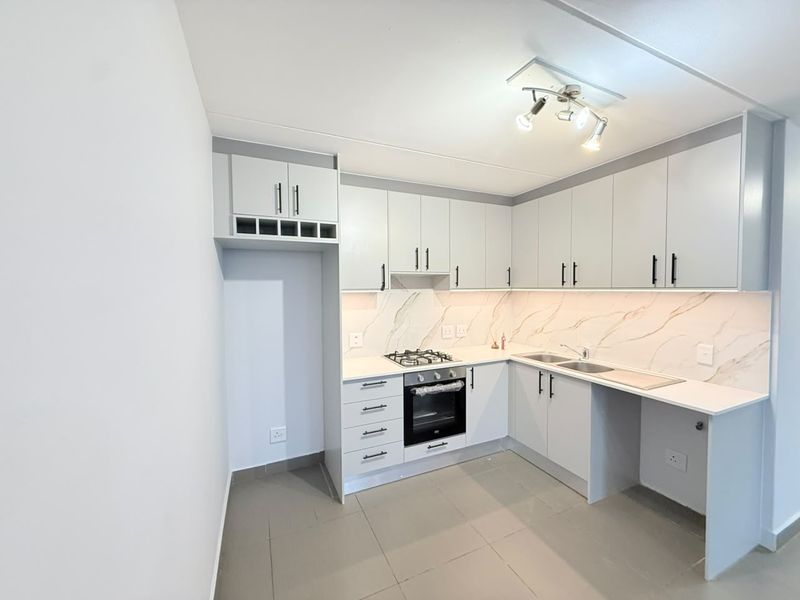 A modern, clean kitchen featuring light grey cabinetry, marble-look splashbacks, a gas hob, built-in oven, and tiled flooring in an open-plan layout.