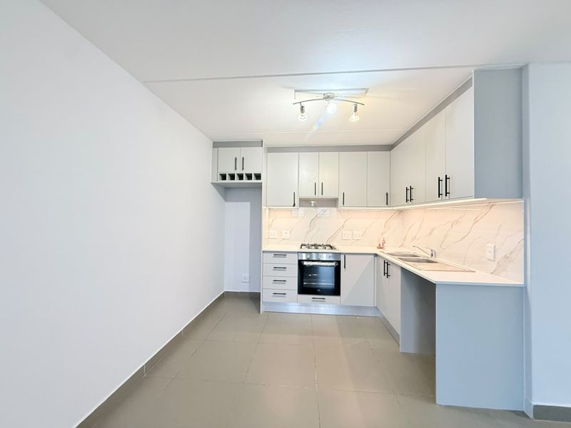 Modern kitchen featuring sleek white cabinetry, marble-look splashback, built-in oven, gas hob, and tiled flooring in a clean, open-plan layout.