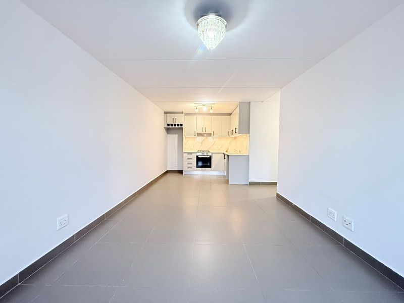 An open-plan living and kitchen area featuring tiled floors, modern cabinetry, and built-in cooking appliances in a clean, vacant space.