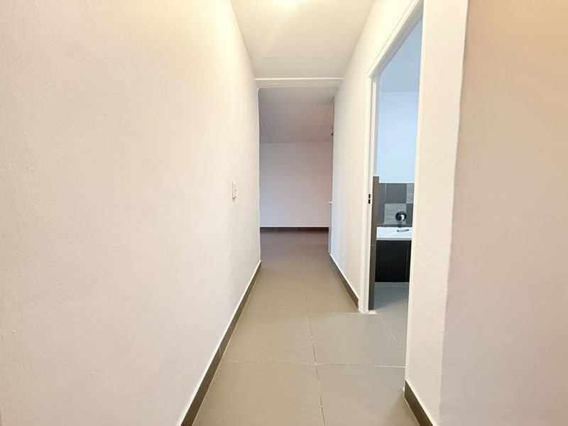 A clean, neutral hallway with tiled flooring leading to an adjacent room and a bathroom.