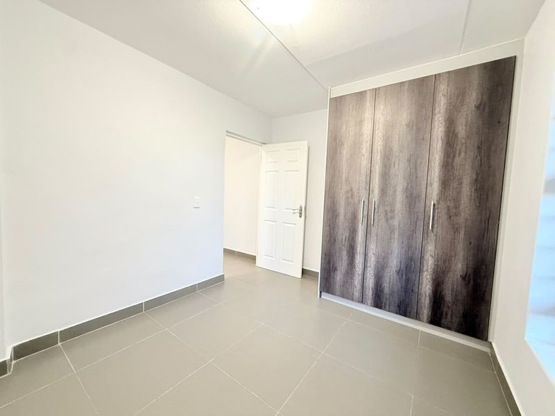 A clean, empty bedroom featuring neutral tiled flooring and modern wood-finish built-in cupboards, offering a versatile space ready for personalization.