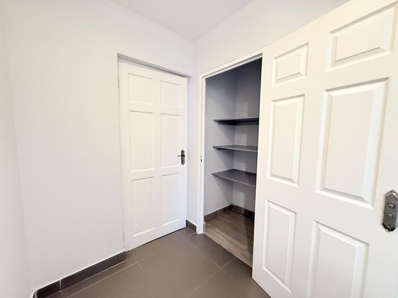 A clean, functional scullery or pantry area featuring built-in shelving, tiled flooring, and white panel doors.