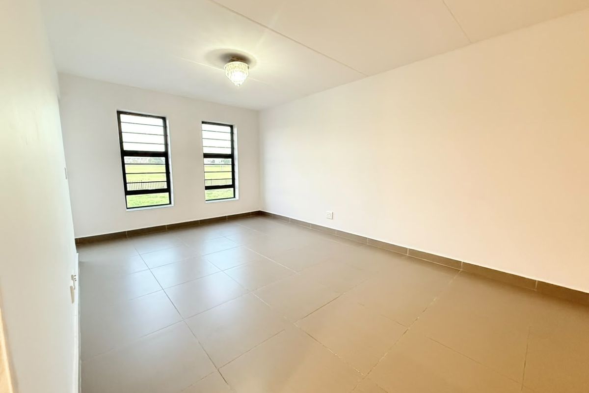 A bright, empty bedroom featuring neutral tiled flooring, large windows with security bars, and a clean, minimalist aesthetic ready for personalization.