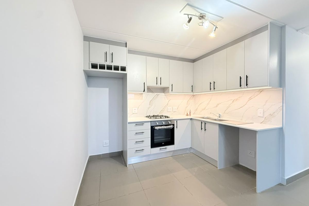 A modern, clean kitchen featuring light grey cabinetry, stone-look backsplash, built-in oven and gas hob, and neutral tiled flooring.