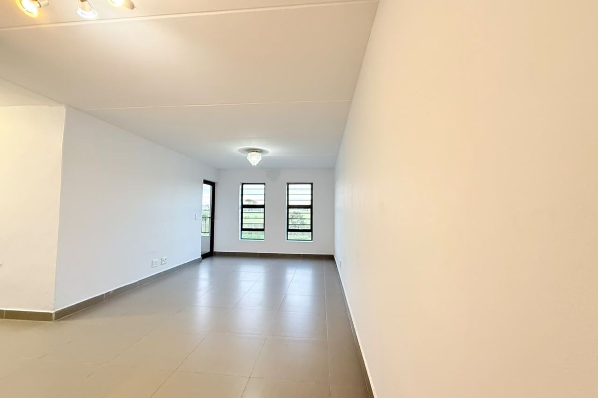 A bright, spacious, and empty living area featuring neutral tiled flooring, modern ceiling lighting, and large windows providing natural light.