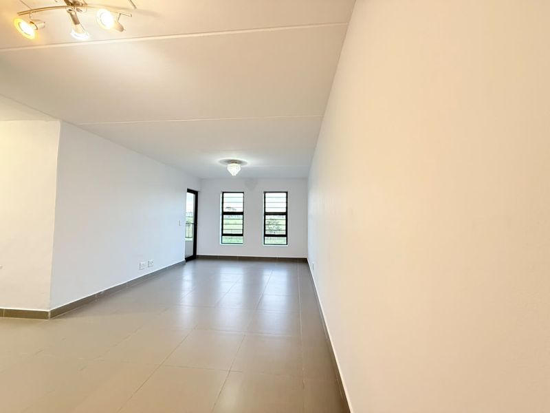 A bright, spacious, and empty living area featuring neutral tiled flooring, modern ceiling lighting, and large windows providing natural light.