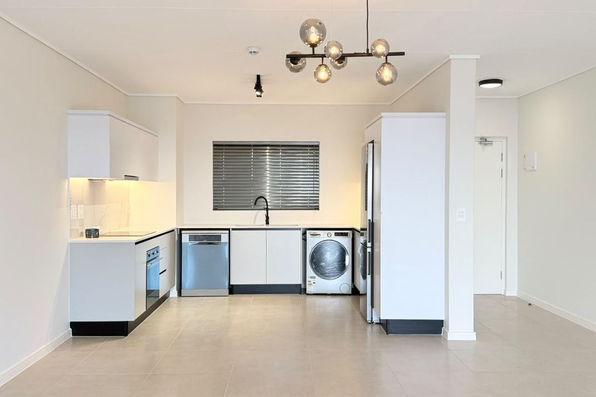 Modern, clean-lined kitchen featuring white cabinetry, integrated appliances, sleek black fixtures, and neutral tiled flooring in an open-plan layout.
