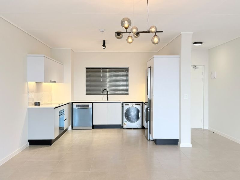 Modern, clean-lined kitchen featuring white cabinetry, integrated appliances, sleek black fixtures, and neutral tiled flooring in an open-plan layout.