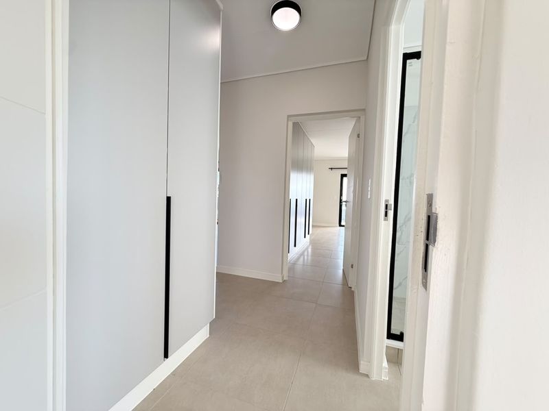 A bright, modern hallway featuring neutral tiled flooring, sleek built-in cupboards with matte black handles, and clean white finishes.
