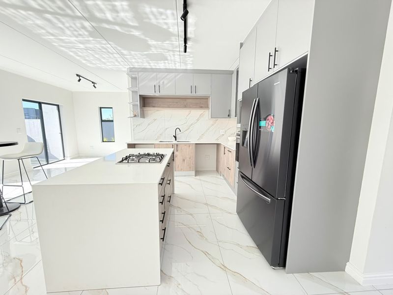 Modern kitchen featuring a central island with a gas hob, sleek cabinetry, marble-look splashback, and high-quality tiled flooring.