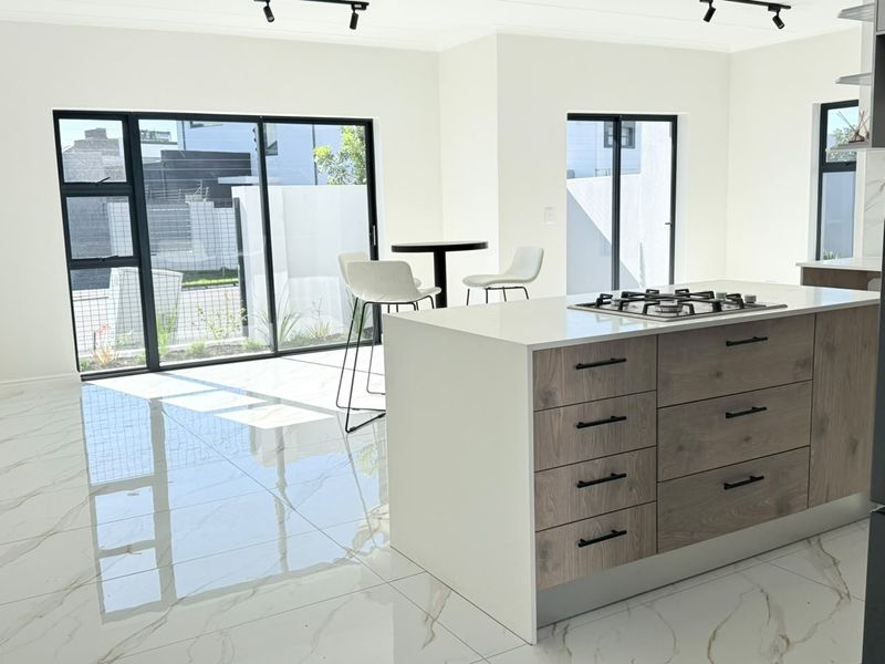 Modern open-plan kitchen and living area featuring a central island with gas hob, sleek cabinetry, and large sliding doors opening to the exterior.