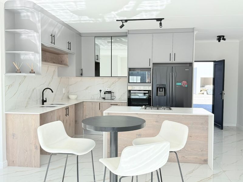 Modern kitchen featuring light wood and grey cabinetry, quartz countertops, marble-look backsplash, integrated appliances, and sleek track lighting.