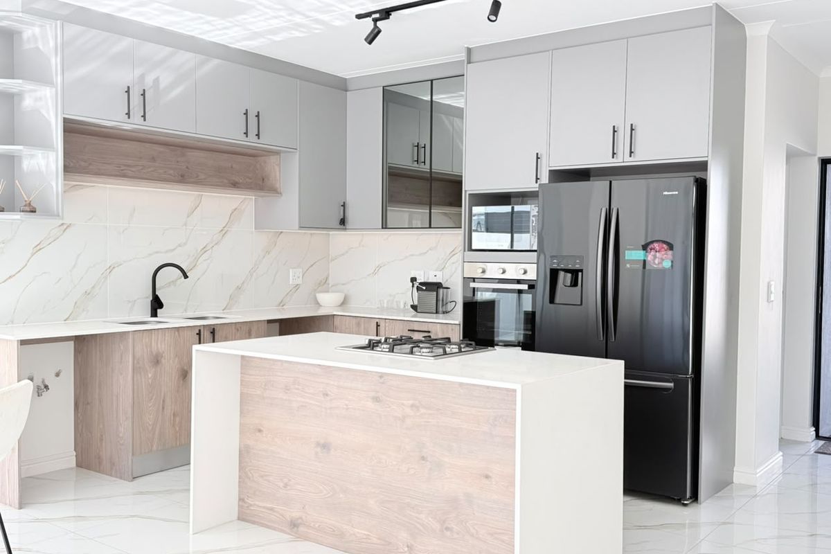 Modern kitchen featuring sleek grey and wood-grain cabinetry, a central island with a gas hob, marble-look splashbacks, and high-quality porcelain floor tiles.