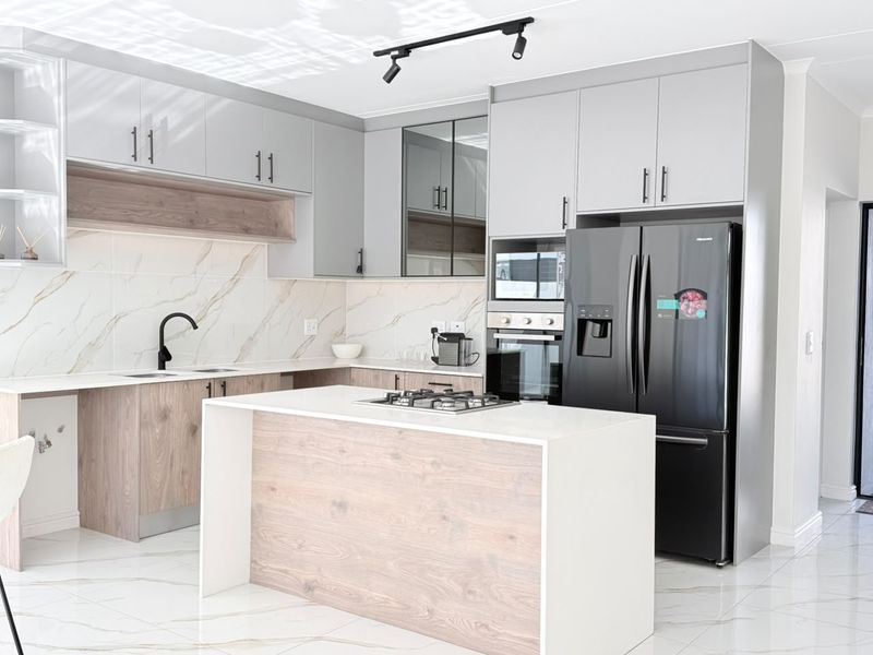 Modern kitchen featuring sleek grey and wood-grain cabinetry, a central island with a gas hob, marble-look splashbacks, and high-quality porcelain floor tiles.