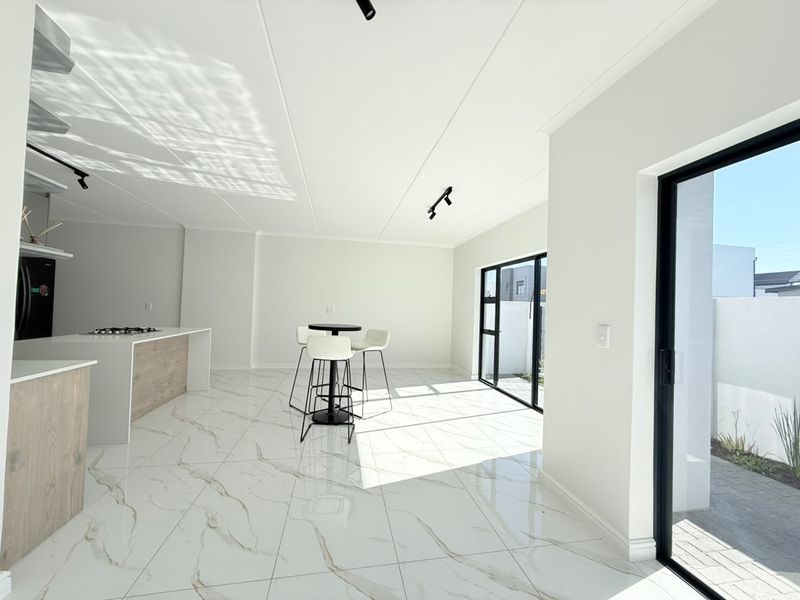 Modern open-plan living and kitchen area featuring high-gloss marble-look floor tiles, a sleek kitchen island with gas hob, and large black aluminium sliding doors.