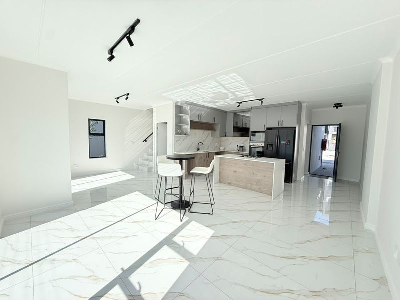 Modern open-plan kitchen and living area featuring marble-look tiled flooring, sleek cabinetry, a central island, and contemporary track lighting.