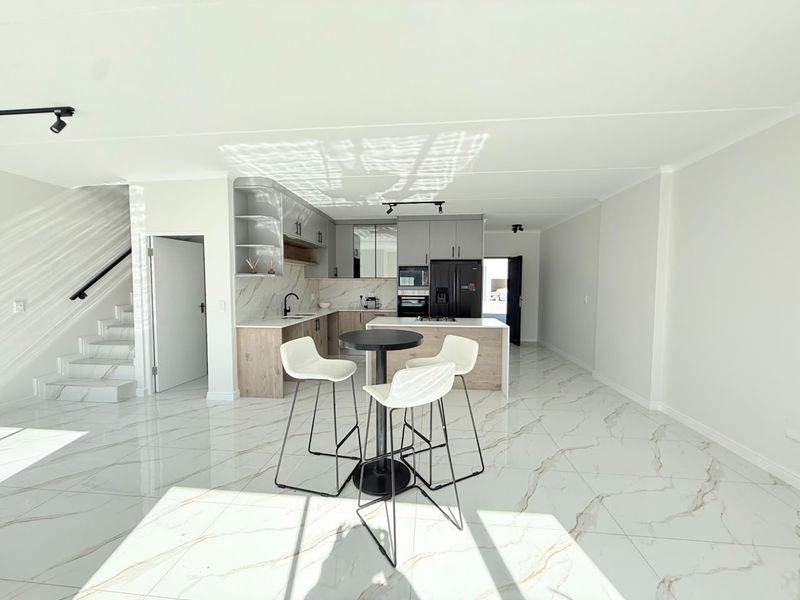 Modern open-plan living area featuring high-gloss marble-look floor tiles, a contemporary kitchen with stone countertops, built-in appliances, and an adjacent staircase.