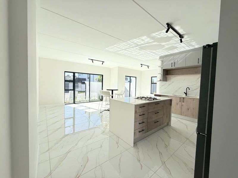 Modern open-plan kitchen and living area featuring a central island with gas hob, marble-look tiled flooring, and sleek cabinetry with contemporary finishes.