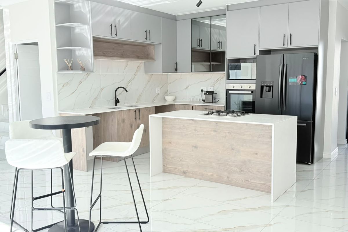 Modern kitchen featuring two-tone cabinetry, stone countertops, a central island with a gas hob, and high-end built-in appliances with marble-look splashback.
