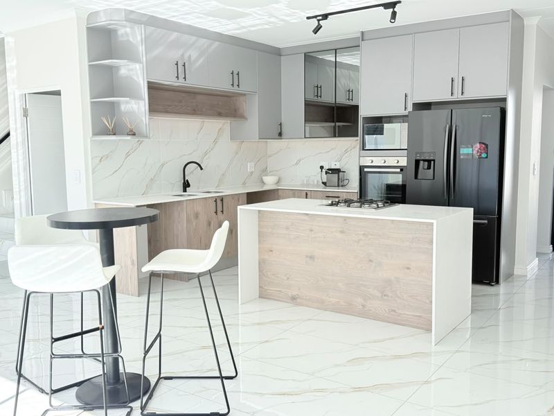 Modern kitchen featuring two-tone cabinetry, stone countertops, a central island with a gas hob, and high-end built-in appliances with marble-look splashback.