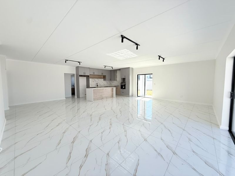 Spacious open-plan living area featuring high-gloss marble-look floor tiles, modern kitchen cabinetry with an island, and abundant natural light through sliding glass doors.