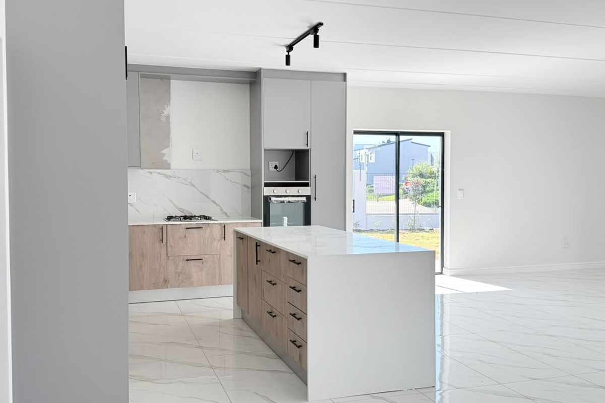 Modern open-plan kitchen featuring a central island, quartz countertops, built-in oven, gas hob, and sleek marble-look floor tiles with direct access to the outdoors.