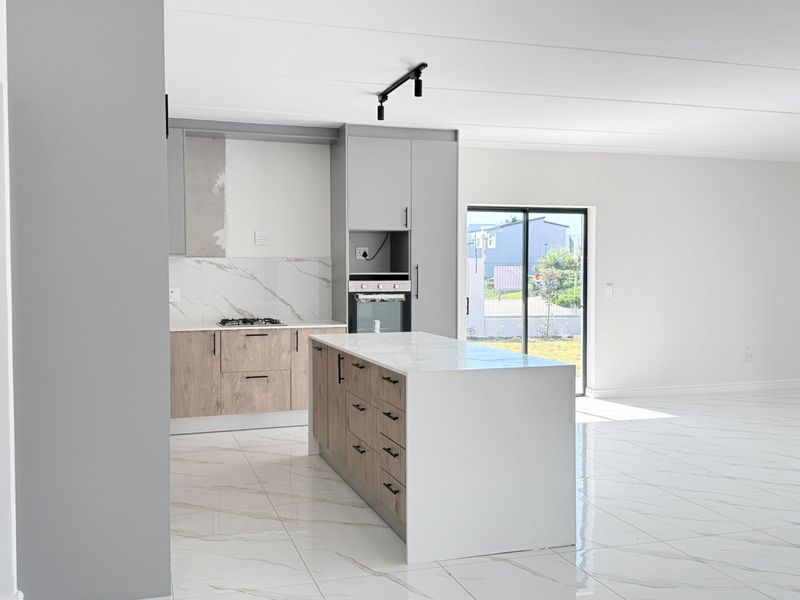 Modern open-plan kitchen featuring a central island, quartz countertops, built-in oven, gas hob, and sleek marble-look floor tiles with direct access to the outdoors.